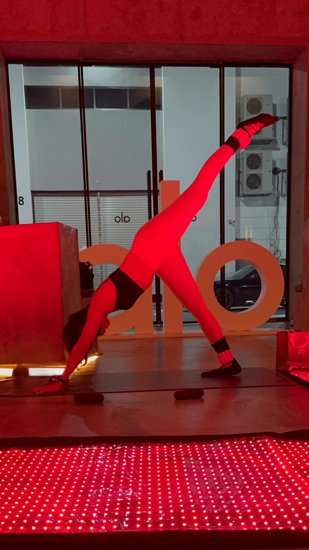 Ciarra holding a standing split on a mat under red light at a Pilates event